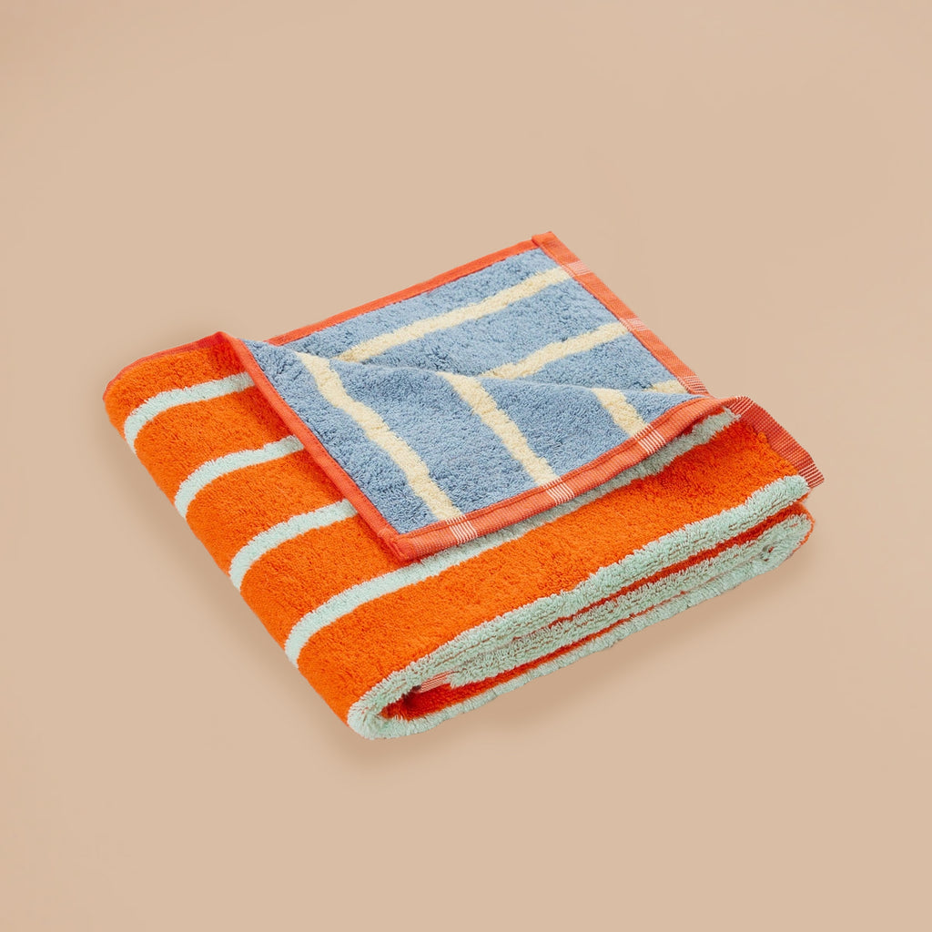 Stone Stripe Hand Towel by Dusen Dusen – folded towel showcasing orange with light blue stripes and blue with cream stripes, displayed on a beige background.
