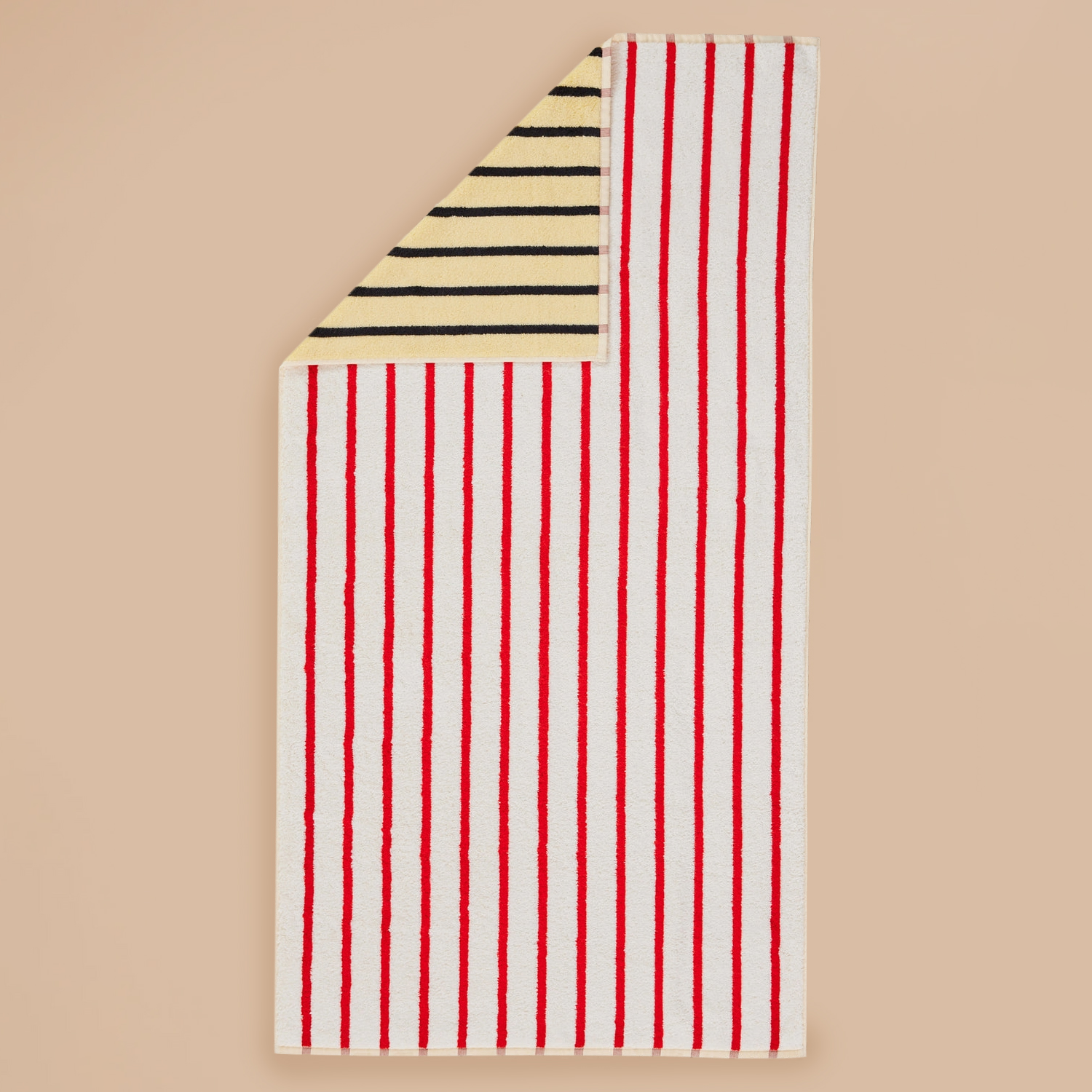 Stucco Stripe Towel by Dusen Dusen – red and white striped towel with a contrasting yellow and black striped reverse, shown flat on a beige background.