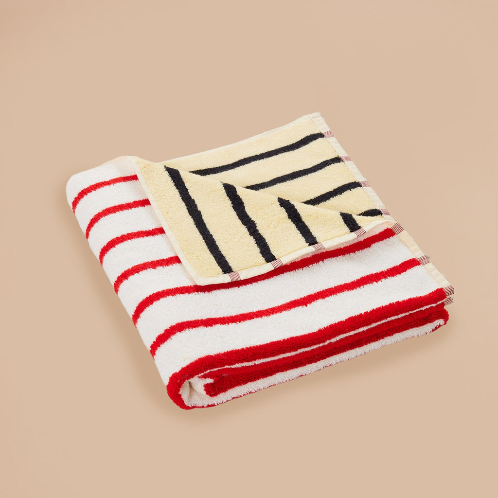 Stucco Stripe Towel by Dusen Dusen – folded towel featuring red and white stripes on one side and yellow with black stripes on the reverse, displayed on a beige surface.
