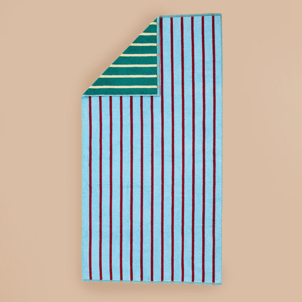 Tile Stripe Bath Towel by Dusen Dusen – a blue towel with burgundy stripes on one side and green with yellow stripes on the reverse, displayed flat on a beige background.
