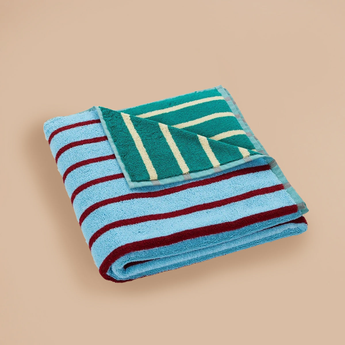 Tile Stripe Bath Towel by Dusen Dusen – folded towel showcasing blue with burgundy stripes and green with yellow stripes, displayed on a beige background.