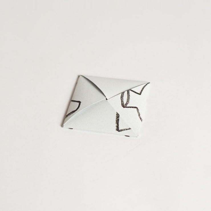 Back view of the pépite origami-style gift card in its folded form, showcasing a clean and minimalist design with crayon-style black details.