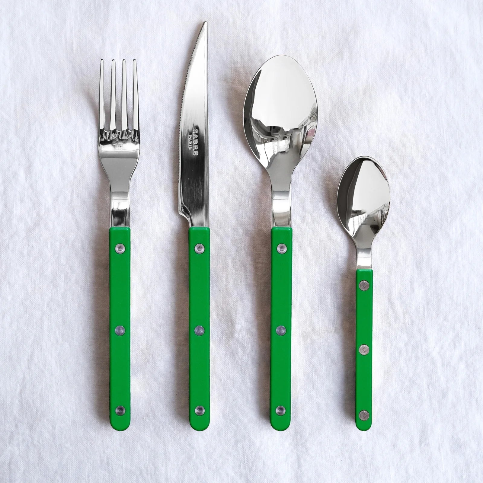 Sabre Paris Bistrot Solid 4-piece cutlery set displayed on a white cloth, showcasing vibrant garden green handles and polished stainless steel tops.