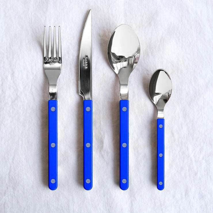 Bistrot Solid 4-piece cutlery set in Lapis Blue by Sabre Paris, including a knife, fork, spoon, and teaspoon with deep blue handles and polished stainless steel tops.