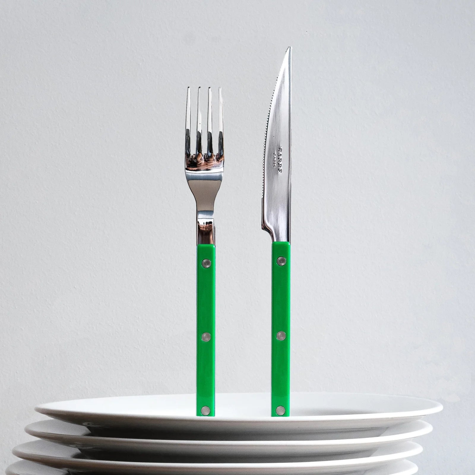 Sabre Paris Bistrot Solid knife and fork standing upright in a stack of white plates, featuring garden green handles and stainless steel tops.