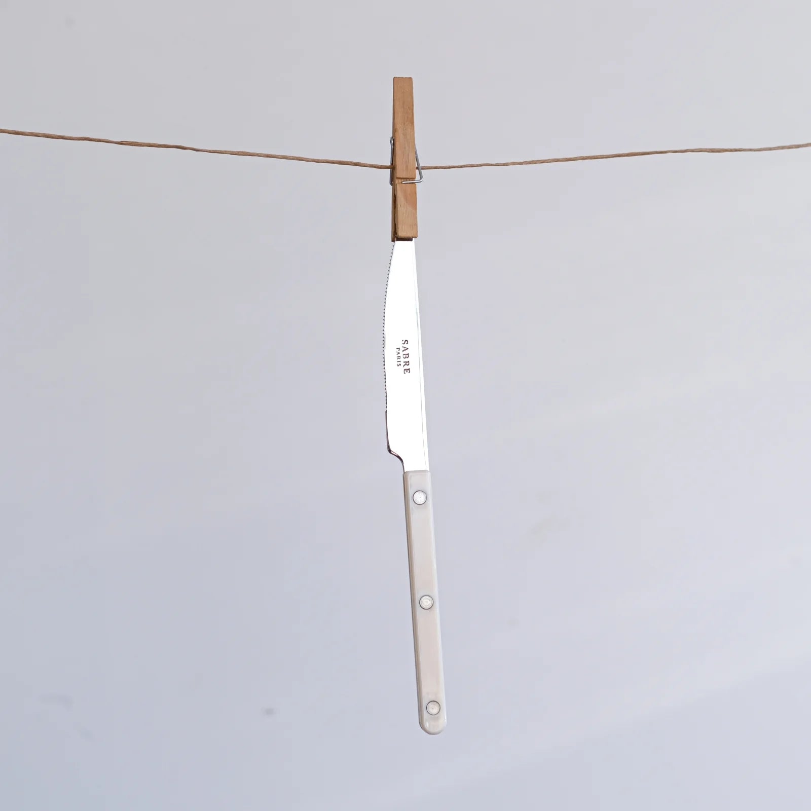 Sabre Paris Bistrot Solid knife with an Ivory handle hanging on a string, highlighting its lightweight yet durable stainless steel blade and riveted design.