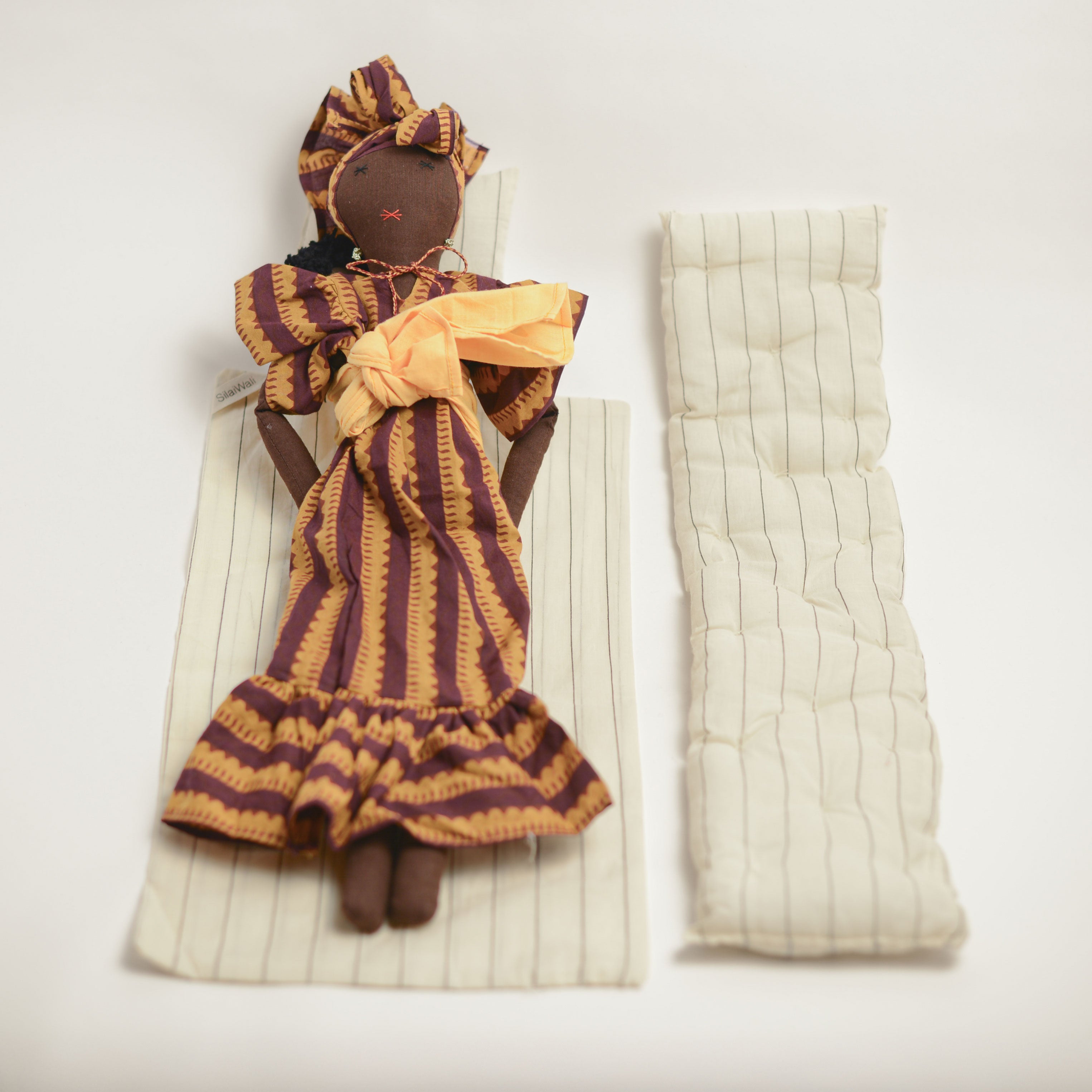 Imani doll by SilaiWali displayed with bedding accessories, featuring striped fabric and detailed craftsmanship.