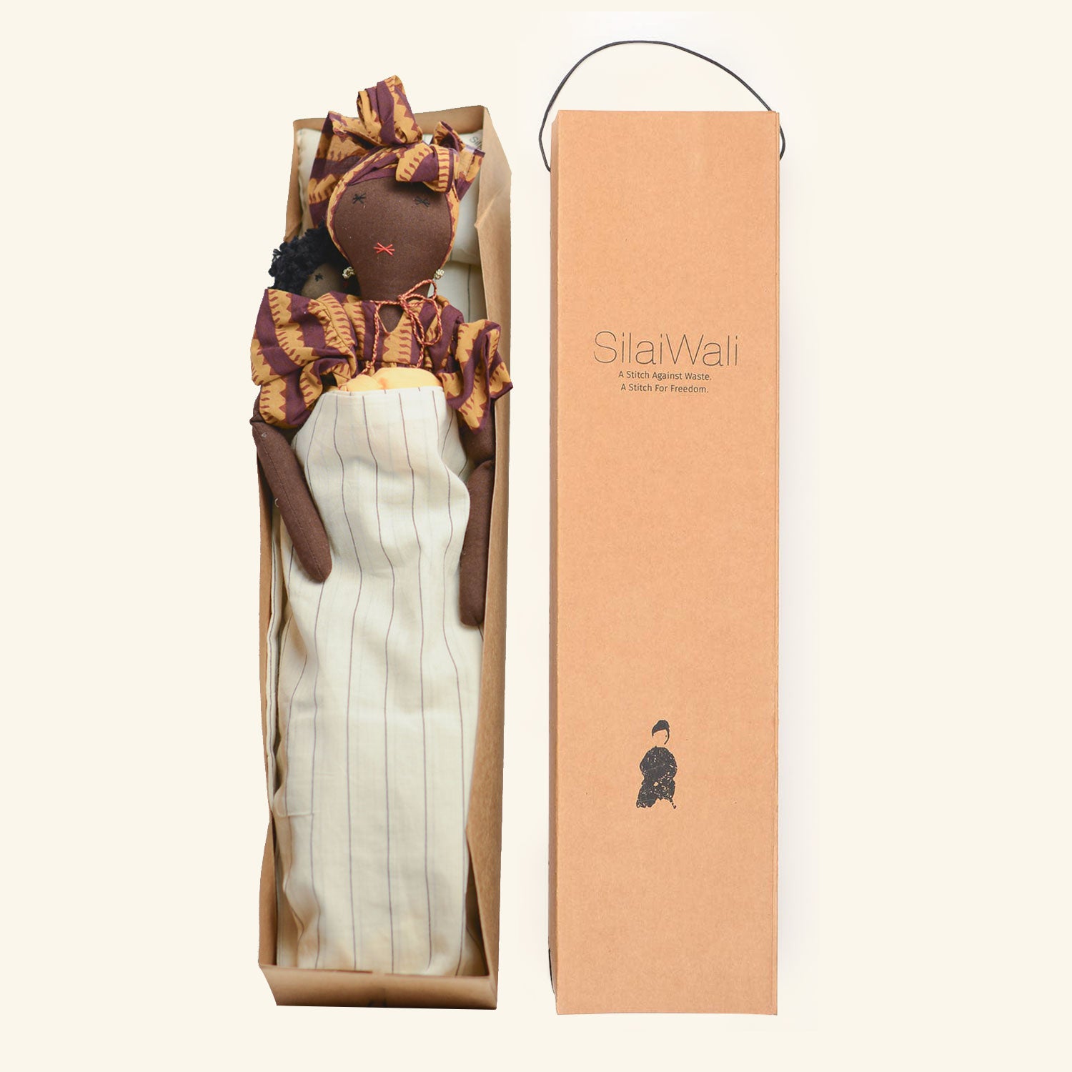 Imani doll by SilaiWali in a cardboard box, showcasing sustainable design with a striped blanket.