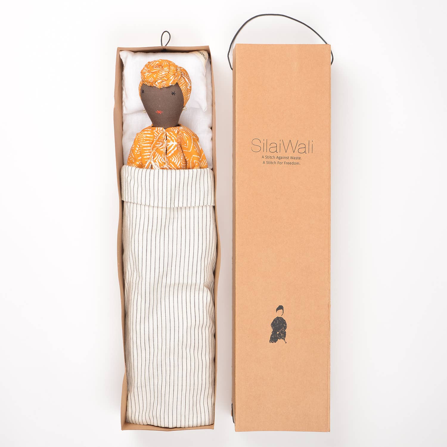 Soumba doll by SilaiWali in a cardboard box, featuring a colourful patterned dress and bedding.