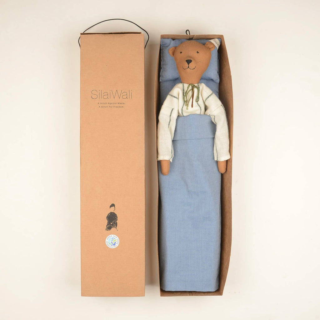 Voda the Bear doll by SilaiWali packaged in a cardboard box, tucked into a blue bedding set, highlighting sustainable design.