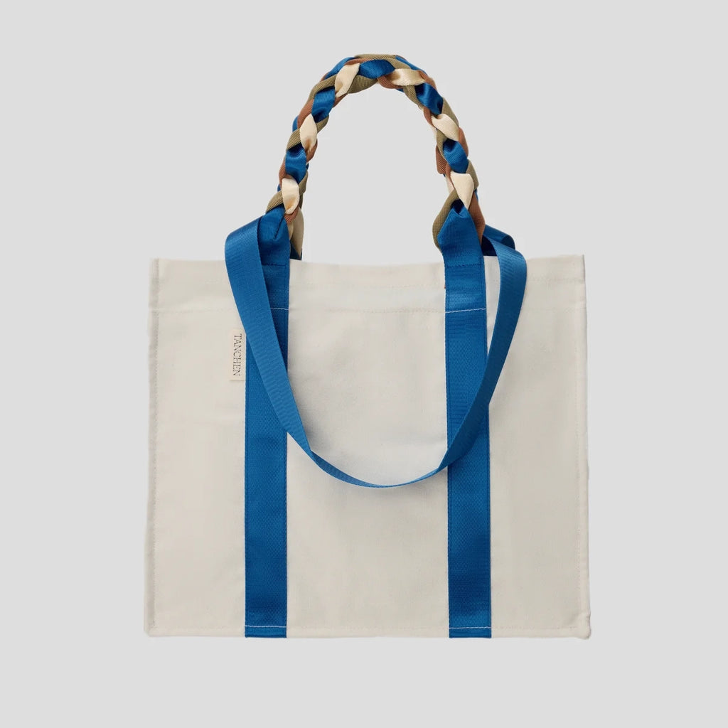 Front view of the Picnic Bag Glou! by Tanchen, showcasing its cream cotton canvas and vibrant blue and brown nylon ribbon handles.